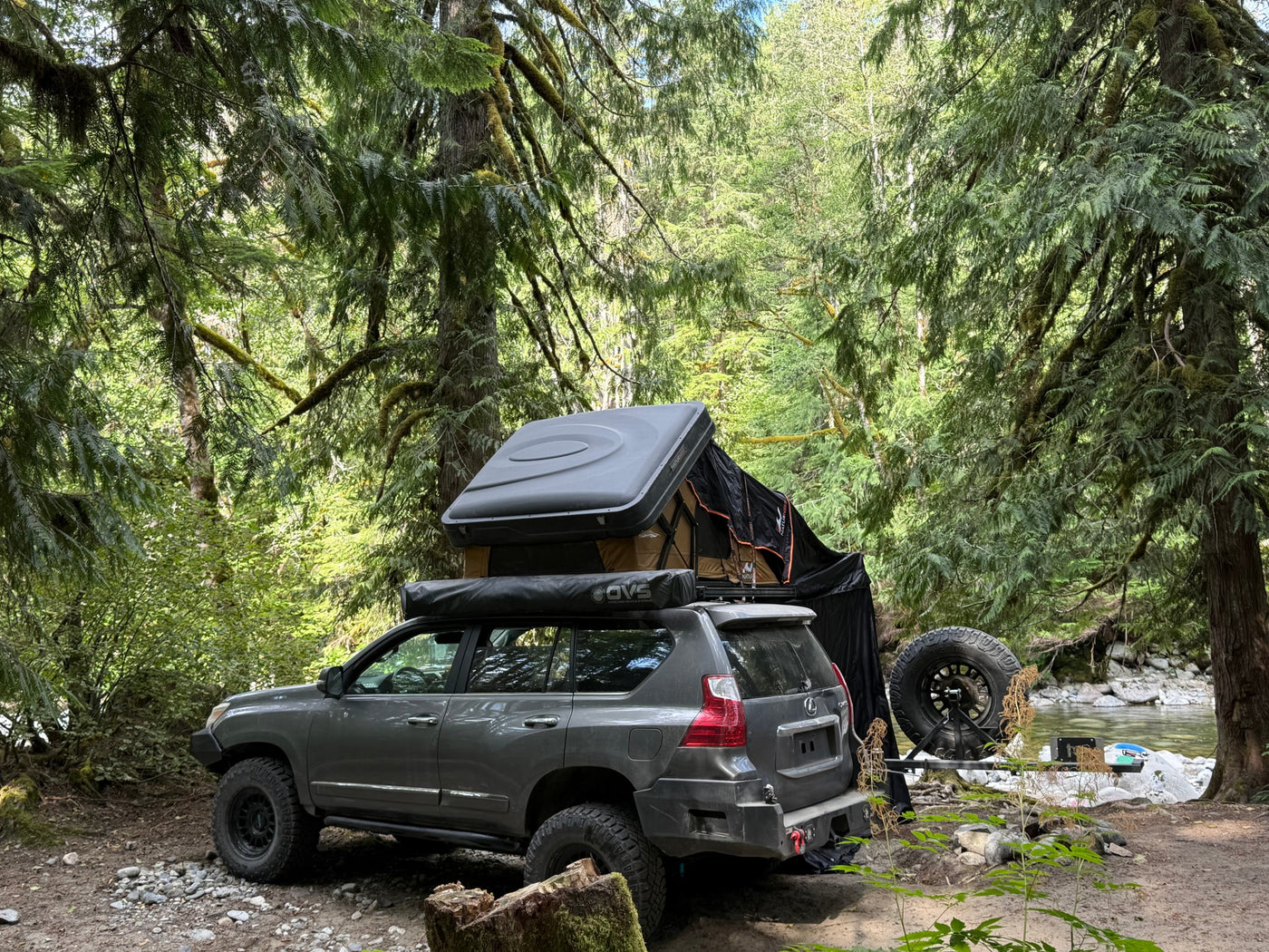 Gray overlanding SUV with rooftop tent & awning by a river. Perfect alternative to traditional RV rental for forest adventures.|Adventure-ready RV rental: A dusty Lexus SUV with a NaturNest rooftop tent by a forest river — photo 4