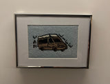 Close-up of a framed cross-stitch artwork, depicting a brown RV with roof details on light blue fabric, ideal for RV rental enthusiasts.