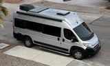 High-angle shot of a silver Ethos RV rental camper van with rooftop solar panels, AC, and all-terrain tires, parked on street.
