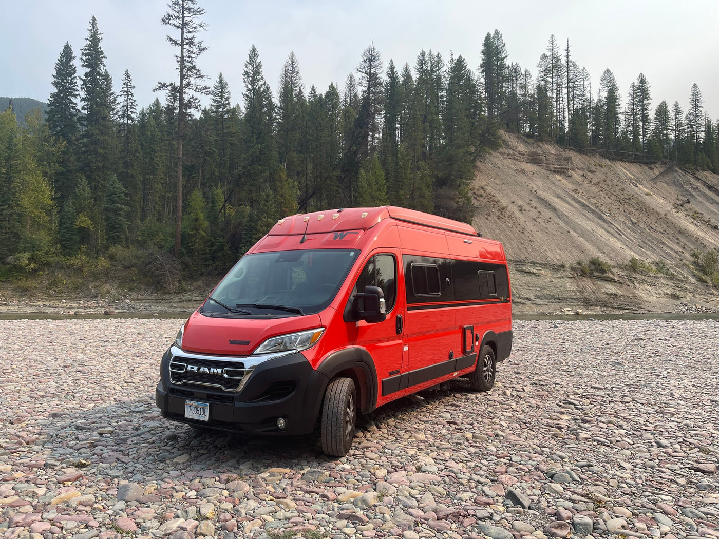  surrounded by forest.|Red camper van RV rental on a rocky riverbed — photo 4