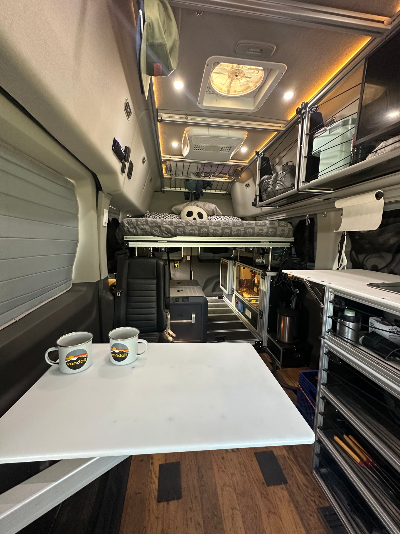 Modern RV rental interior: a comfy camper van with dining table, skull-patterned elevated bed, ample storage, and ceiling fan.