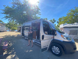 Man with dog by a silver RV rental at a sunny lakeside campsite, perfect for a summer road trip.