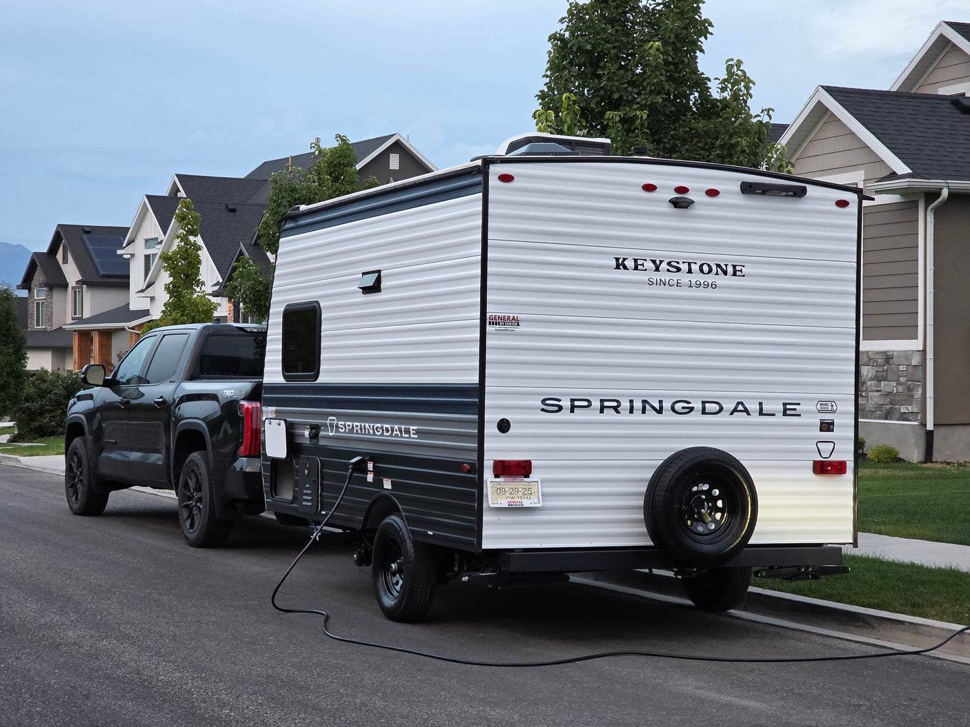 An RV rental: A Keystone Springdale travel trailer is hitched to a pickup truck, parked on a residential street.
