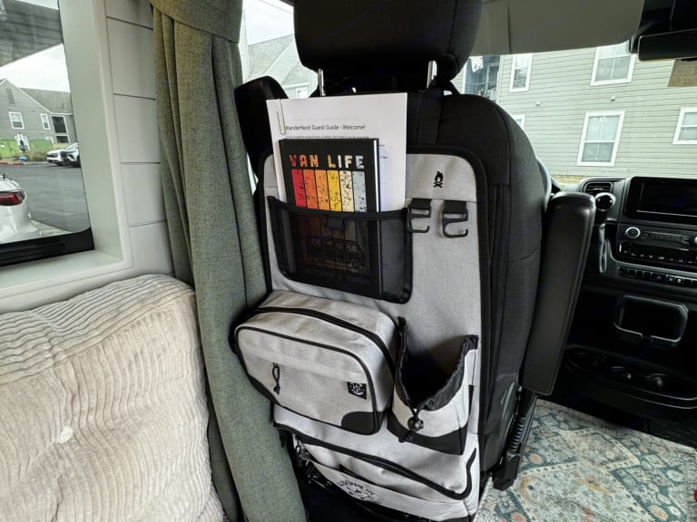 RV rental interior: A seat-back organizer with a "VAN LIFE" book and guest guide ensures essentials are handy for your journey.