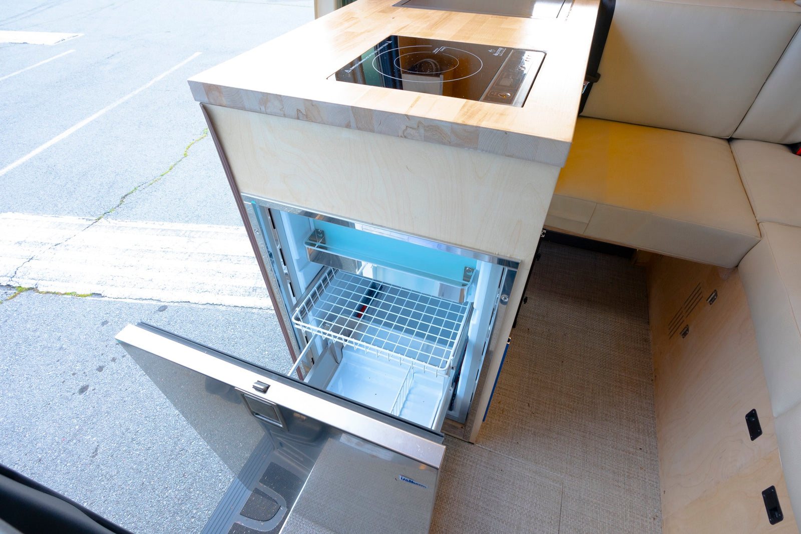 RV rental kitchen: open compact fridge, induction cooktop, and custom wood cabinetry. Perfect for road trips.