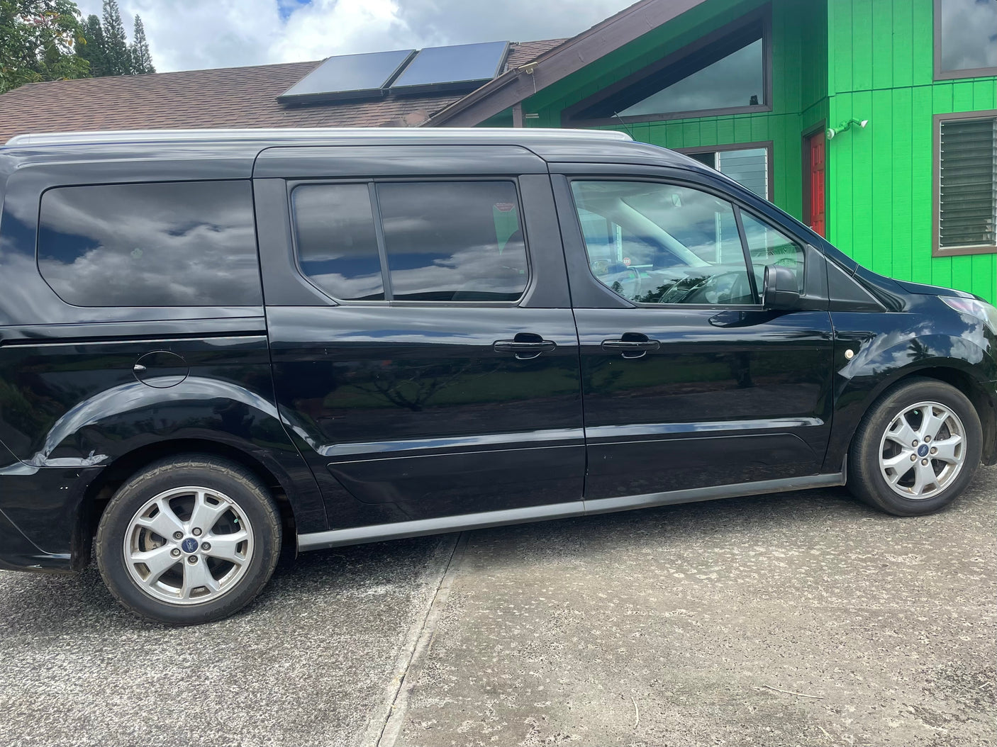 Black van, an ideal RV rental option for travel, parked beside a vibrant green home with roof solar panels.