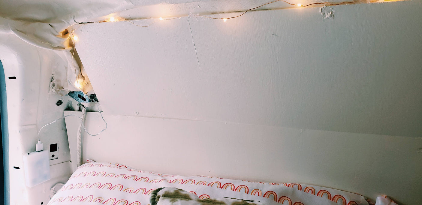 Cozy RV rental interior with a bed, rainbow pillow, and warm fairy lights, ideal for a comfortable road trip.