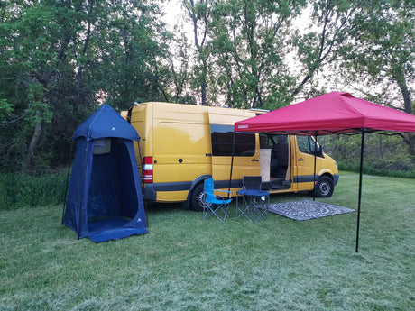 Yellow RV rental van parked on grass with a blue shower tent and red canopy setup, perfect for outdoor camping.