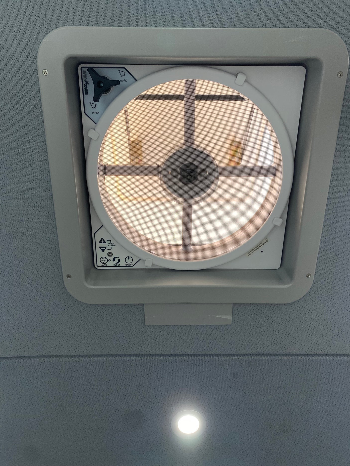 Overhead MaxxFan ceiling vent in an rv rental interior, showing its screen, controls, and a recessed ceiling light.
