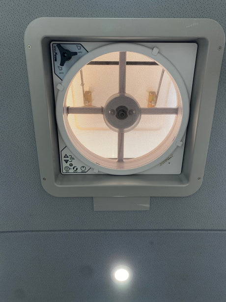 Overhead MaxxFan ceiling vent in an rv rental interior, showing its screen, controls, and a recessed ceiling light.