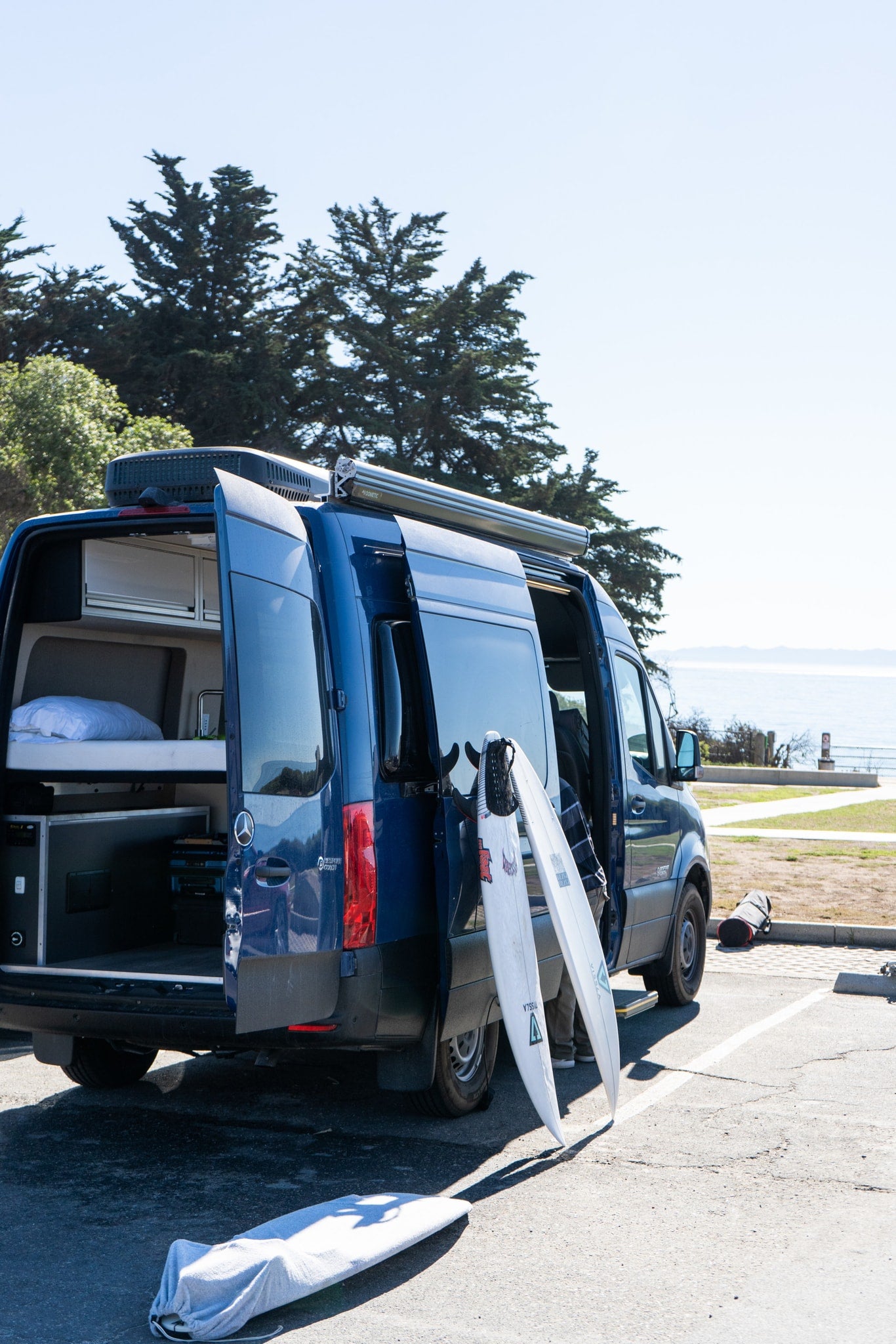 An RV rental van with open doors, surfboards leaning against it, parked at a coastal overlook. — photo 9