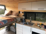 This RV rental's interior boasts a cozy elevated bed & functional kitchen with a sink, perfect for compact van life adventures.
