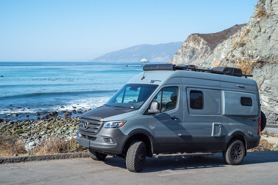 A grey Mercedes-Benz Sprinter RV rental parked at a scenic coastal overlook, with clear blue ocean and rocky shore. — photo 14