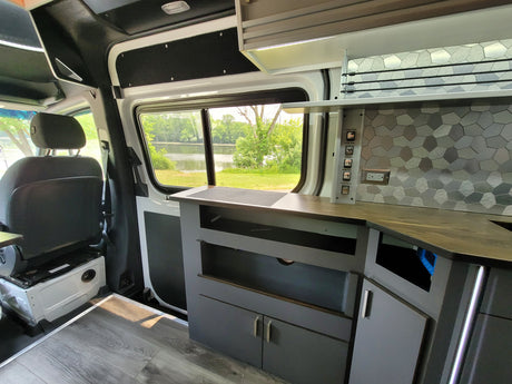 Spacious custom camper van interior for your next RV rental adventure, featuring a kitchen, cozy seating, & nature views.