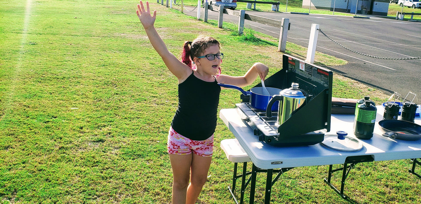Young girl stirring food on a portable stove while camping. Perfect for an RV rental adventure!