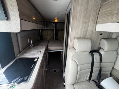 Explore the cozy interior of an rv rental: a kitchenette, convertible bed, and passenger seating ready for your next road trip.