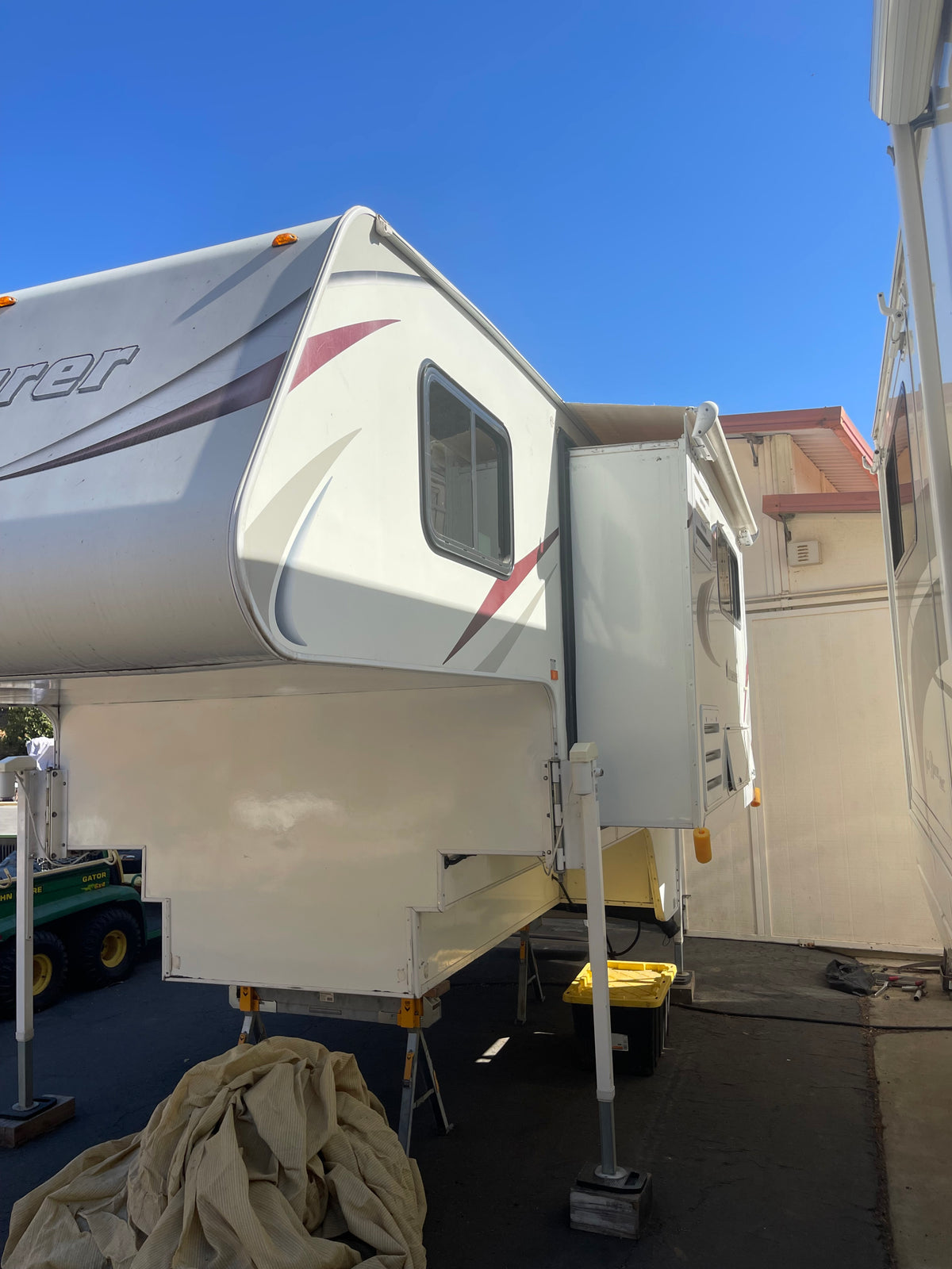 An elevated white RV rental, a truck camper, stands outdoors with its slide-out extended under a clear blue sky. — photo 2
