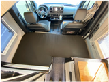 Inside an rv rental camper van: a black mattress forms a bed, stretching towards the cockpit with steering wheel visible.