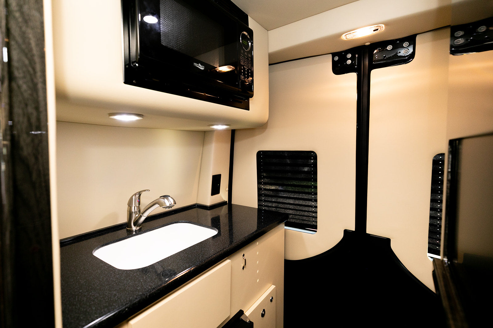 RV rental interior: Compact kitchen with sleek microwave, sink, and black countertop. Brightly lit for easy use.