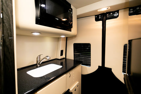 RV rental interior: Compact kitchen with sleek microwave, sink, and black countertop. Brightly lit for easy use.