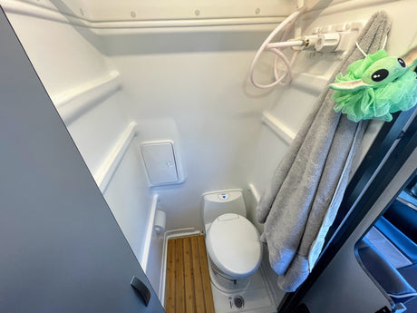 Inside an **rv rental**: a modern wet bath with shower, toilet, and wooden mat for comfortable travels.