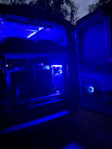 Blue-lit RV rental interior at night, showcasing a custom computer setup. Perfect for unique tech travel experiences.