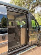RV rental: Modern camper van with screen door open, revealing a person working on a laptop inside, parked in nature.