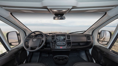 RV rental: Inside a camper van's cockpit, showing the dashboard, steering wheel, and a scenic waterfront view ahead.