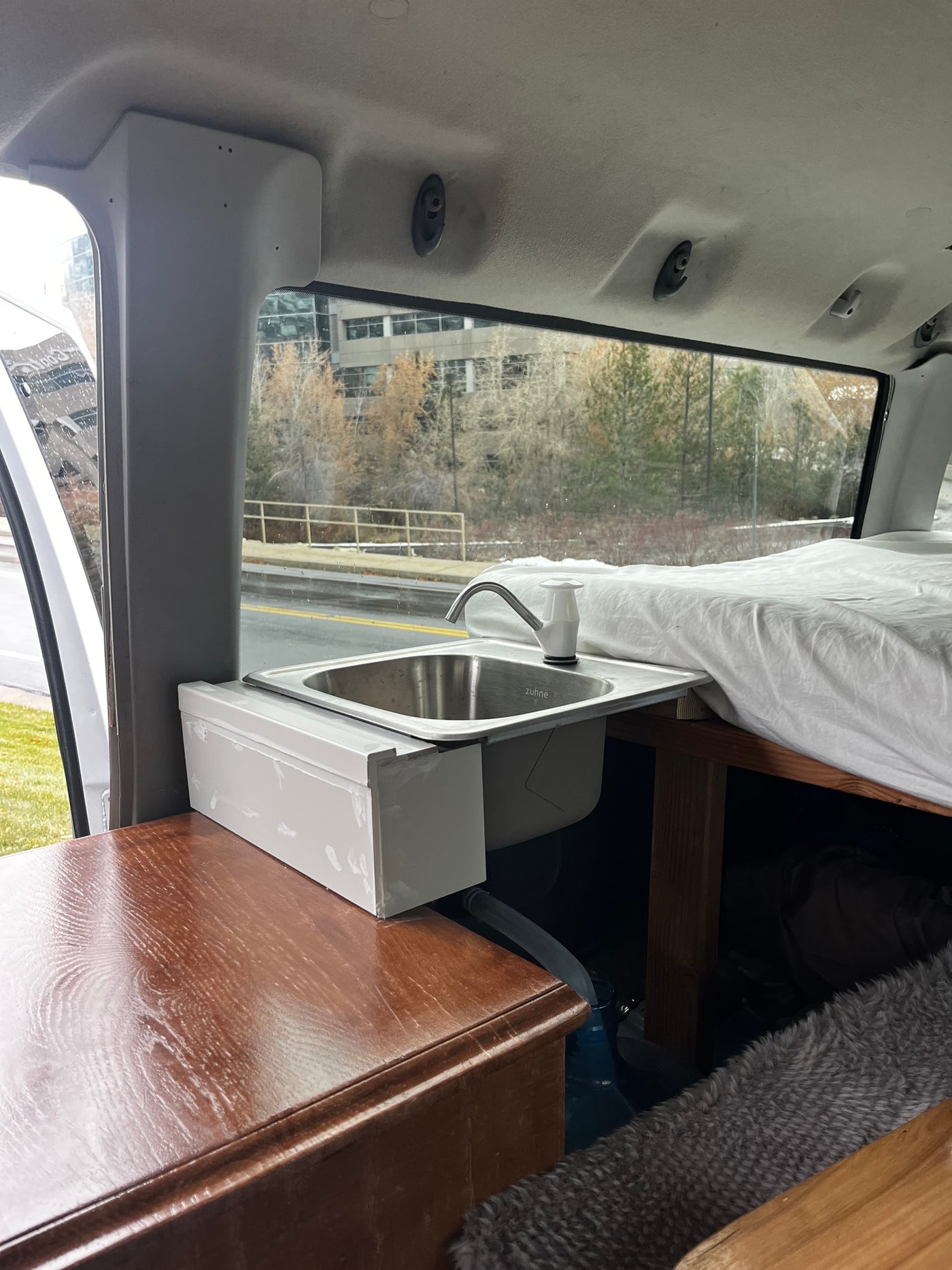 Inside an RV rental: a compact camper van kitchenette with a ZUHNÉ sink and faucet, next to a cozy bed. — photo 11