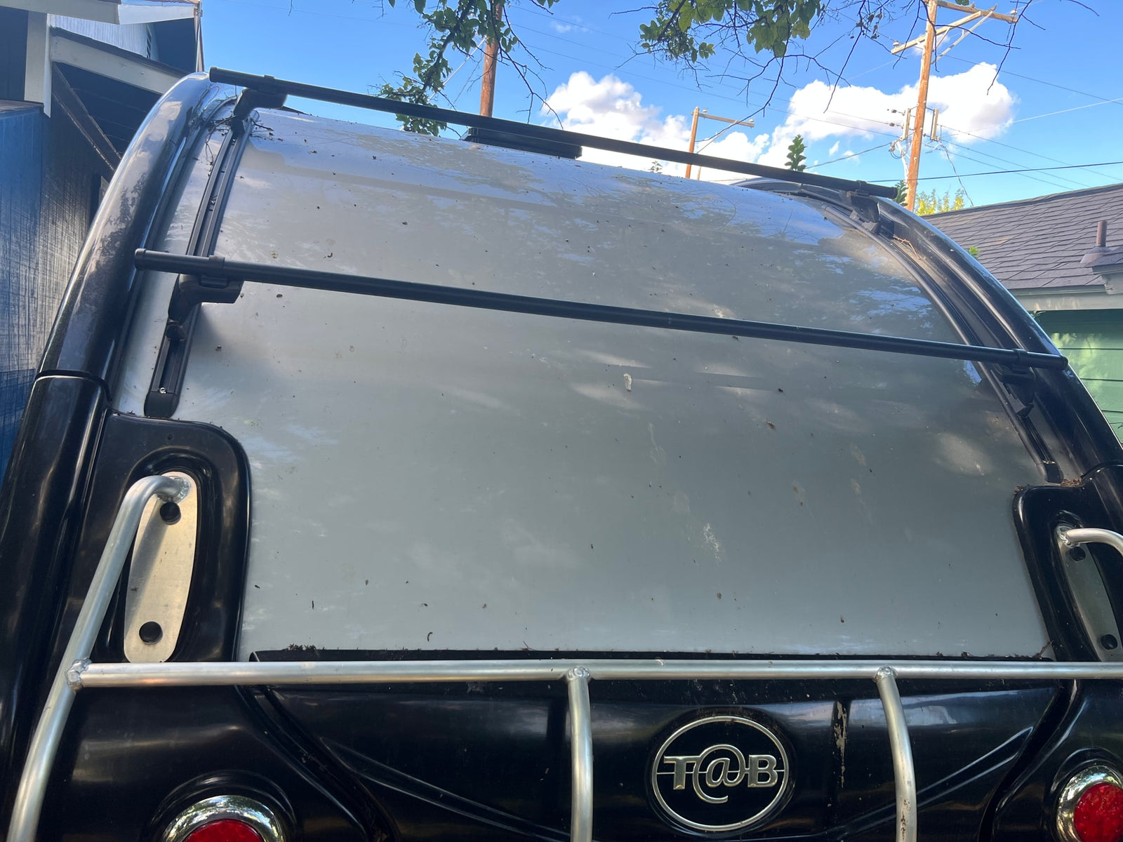 Rear view of a T@B camper with a roof rack, featuring a light grey roof and black body, ideal for rv rental.