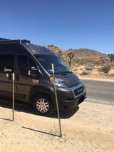 A dark grey Ram ProMaster rv rental campervan parked on a dirt shoulder in a sunny desert with Joshua trees.