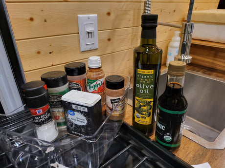 RV rental kitchen: cooking essentials like olive oil, spices, & soy sauce neatly arranged by the sink.