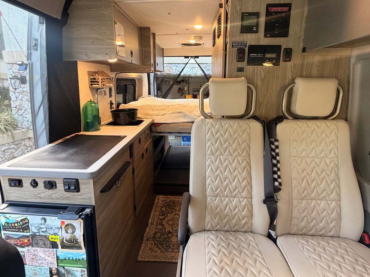  is parked on a dark driveway with palm trees under a blue sky.|White Winnebago Solis RV rental camper van with pop-top open — photo 6