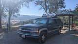 Dark green SUV, packed with gear, at a scenic campsite overlooking a valley. Great for an outdoor trip like an RV rental.