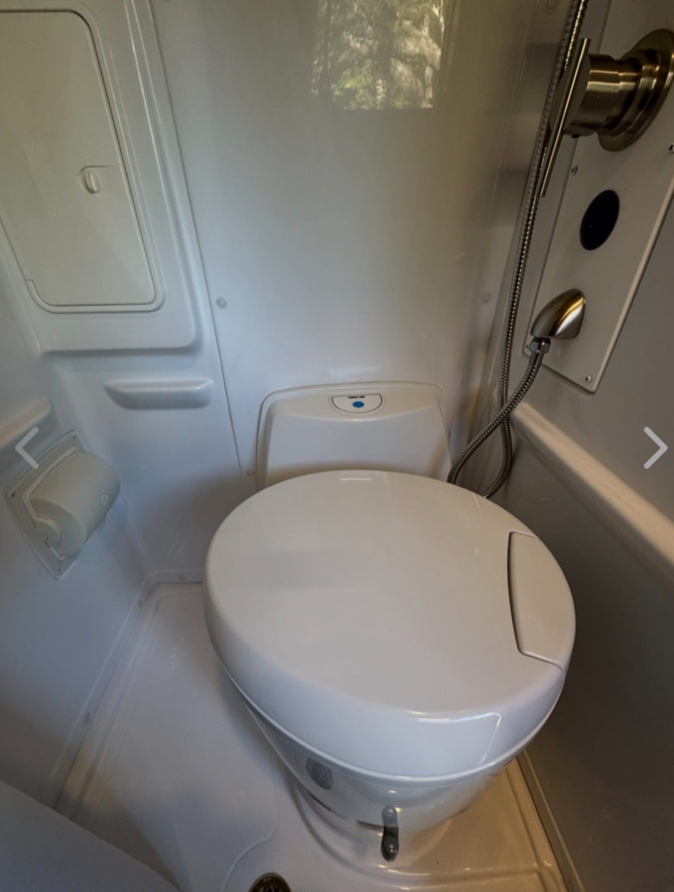 Compact RV rental wet bath with a toilet, shower, and toilet paper holder, demonstrating functional design.