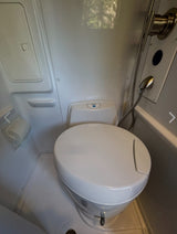 Compact RV rental wet bath with a toilet, shower, and toilet paper holder, demonstrating functional design.