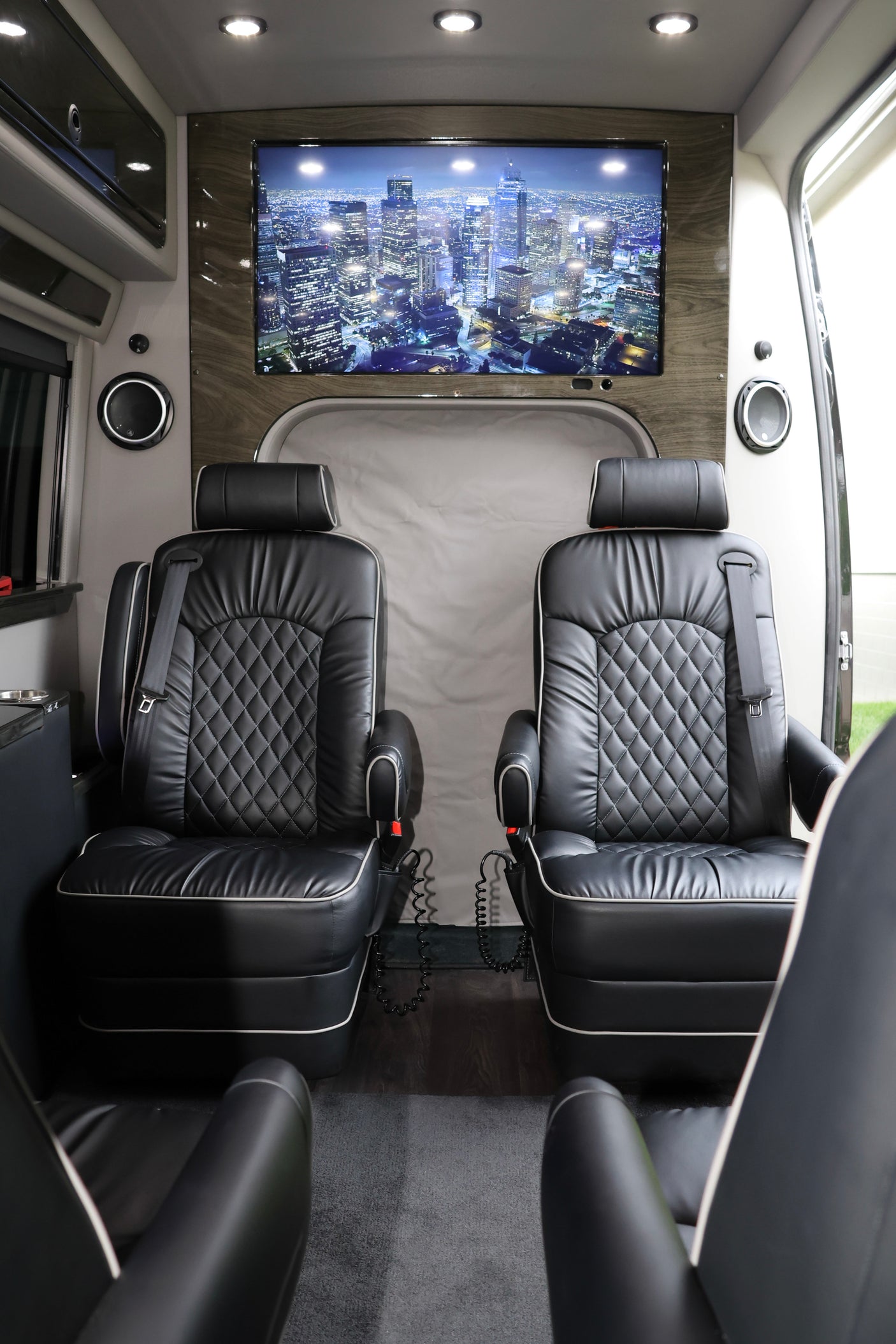 Plush black captain's chairs and a large screen displaying a city skyline define this luxurious rv rental interior.