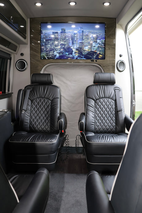 Plush black captain's chairs and a large screen displaying a city skyline define this luxurious rv rental interior.