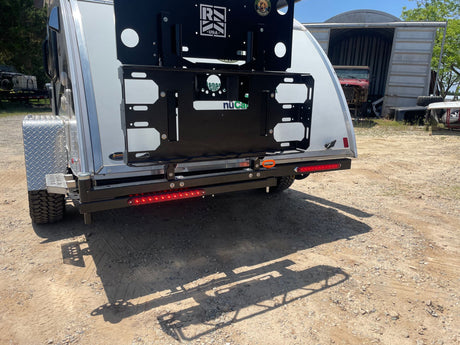 RV rental: Rear of white travel trailer. Features black cargo rack, bright red LED taillights, and off-road tire. Ready for adventure.