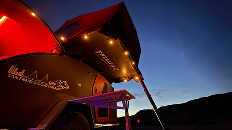 Experience overland camping with this RV rental! Trailer with rooftop tent & bright lights at dusk. San Francisco Overland.