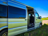 Silver RV rental van parked with its door open, showing interior and reflecting a scenic outdoor landscape.