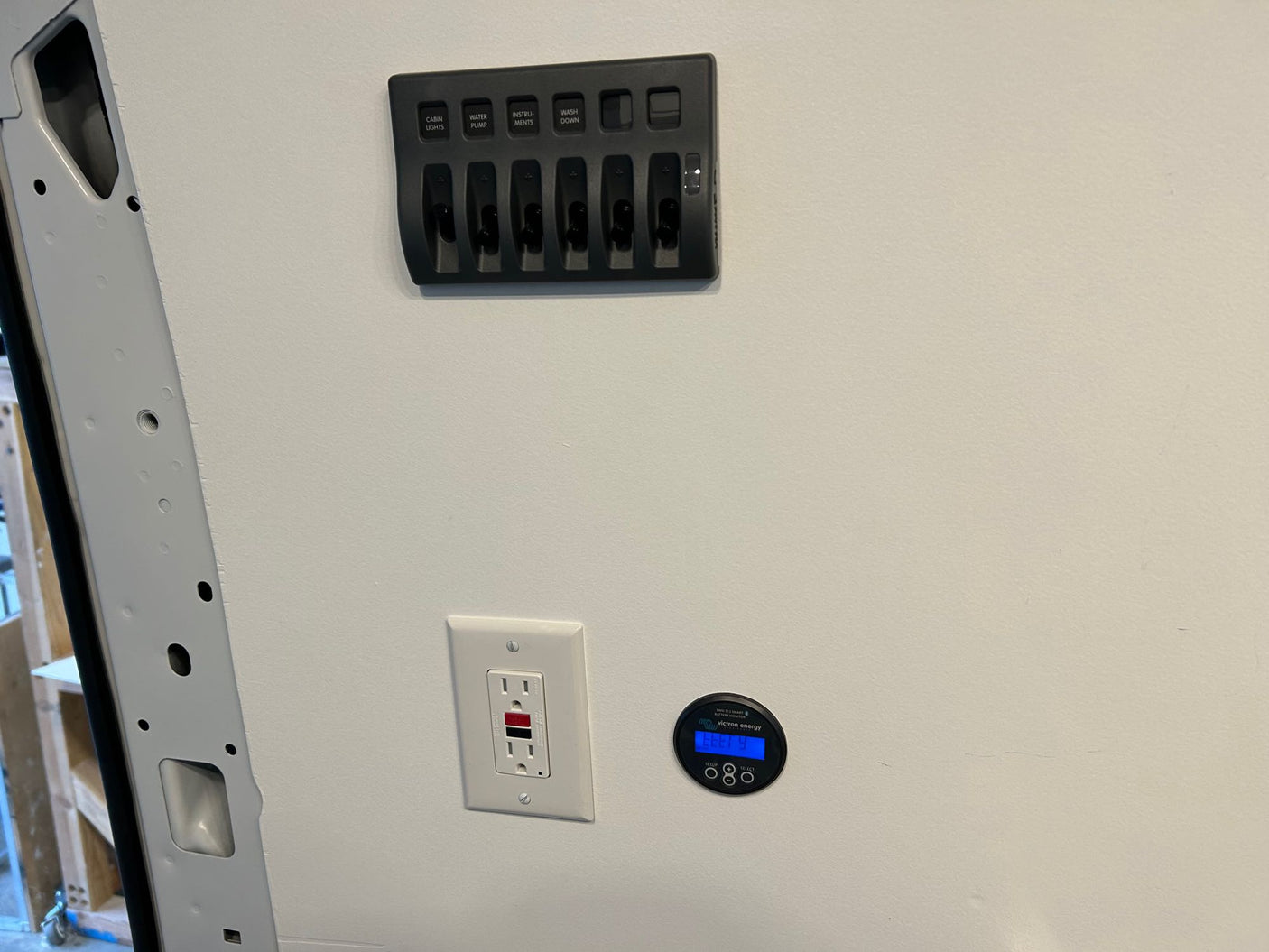 RV rental cabin interior featuring a control panel with switches, an electrical outlet, and a Victron energy battery monitor.
