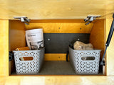Inside an RV rental storage compartment: wooden interior, carpeted floor, two grey baskets, and a "Blue Spruce" guide.