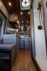 Step inside this cozy RV rental camper van. Features include a comfy bench, kitchen, bed, and built-in shower.