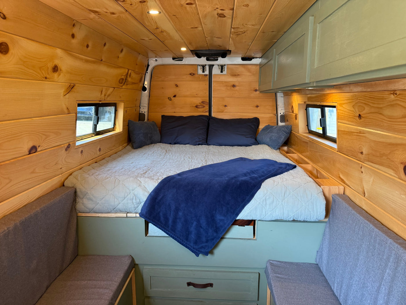 Cozy RV rental interior with a comfortable bed, warm wooden walls, and sage green cabinetry for a perfect camper van experience. — photo 5