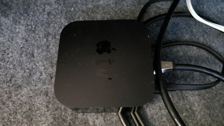 A dusty black Apple TV device, connected to cables on a gray textured surface, ready for your RV rental entertainment.
