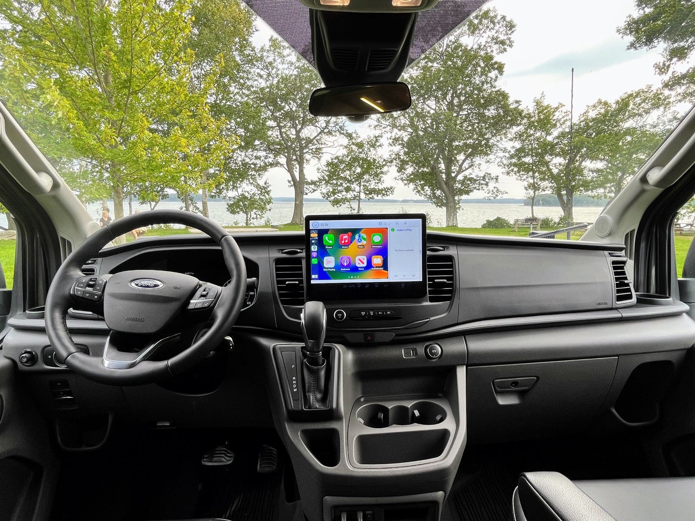 RV rental: Ford van interior featuring a large Apple CarPlay screen, with a scenic lake view outside.