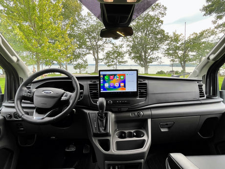 RV rental: Ford van interior featuring a large Apple CarPlay screen, with a scenic lake view outside.