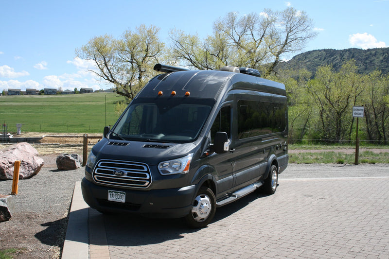 Dark grey Ford Transit van RV rental parked on pavers, with green fields and trees in the background. — photo 4