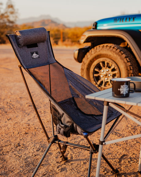 Relaxing outdoor setup: portable chair, table, and mug by a rugged vehicle, ideal for your next RV rental adventure.
